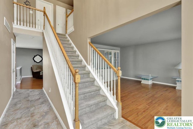 stairway with baseboards, wood finished floors, a towering ceiling, and visible vents