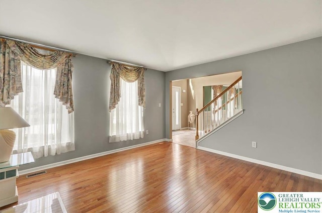 unfurnished living room featuring baseboards, plenty of natural light, stairs, and hardwood / wood-style floors