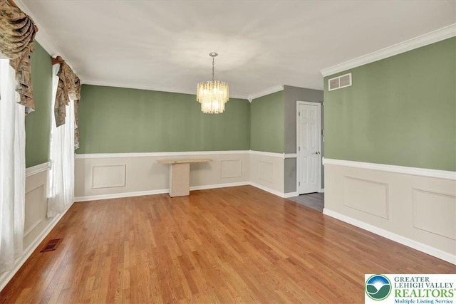unfurnished dining area with visible vents, a decorative wall, wood finished floors, and an inviting chandelier