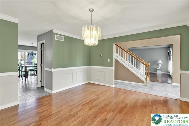 unfurnished dining area with crown molding, visible vents, stairs, wood finished floors, and a notable chandelier