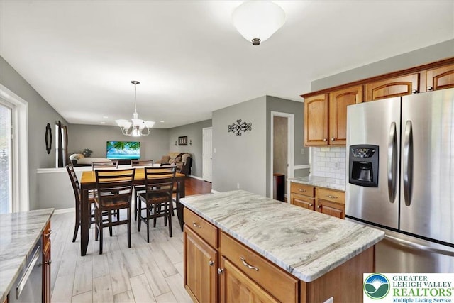 kitchen with light stone countertops, a notable chandelier, stainless steel appliances, open floor plan, and decorative backsplash