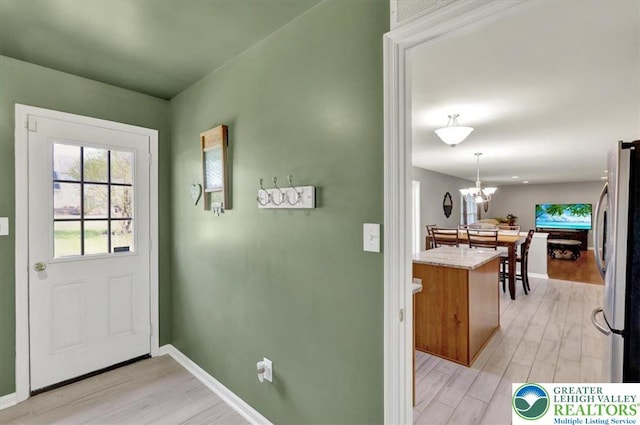 doorway with an inviting chandelier, baseboards, and light wood-type flooring