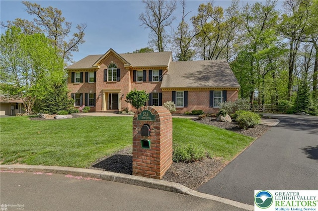 colonial home with brick siding, a front lawn, and fence