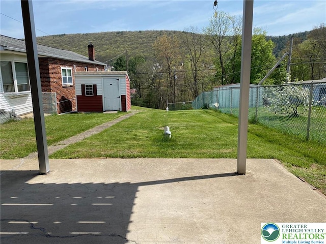 view of yard with fence, an outbuilding, a patio area, and a wooded view