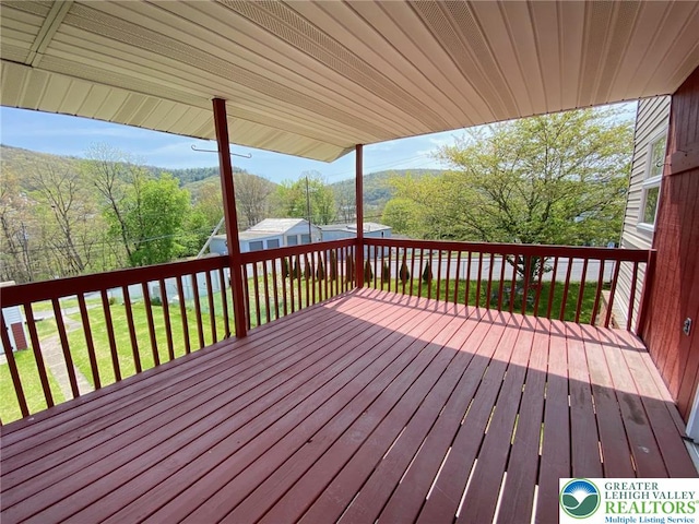 wooden terrace featuring a lawn, a view of trees, an outbuilding, and a storage unit