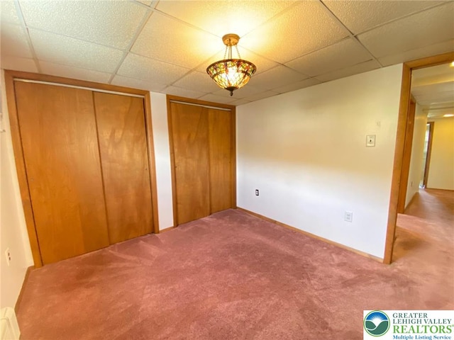 unfurnished bedroom with carpet floors, baseboards, multiple closets, and a drop ceiling