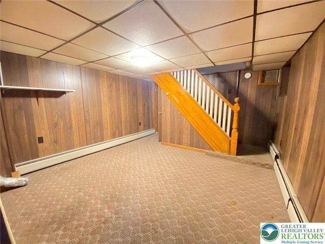 finished below grade area featuring wooden walls, a baseboard heating unit, and a drop ceiling