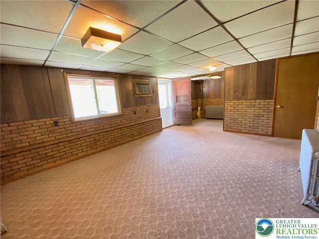 below grade area with radiator, brick wall, wooden walls, and a paneled ceiling
