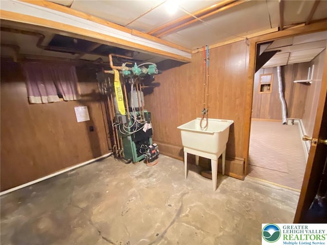 unfinished below grade area with a heating unit, wood walls, and a sink