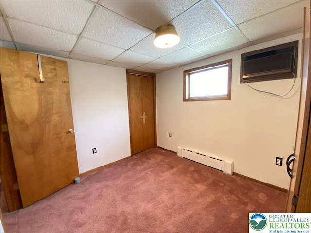 basement with carpet floors, a wall mounted air conditioner, a paneled ceiling, and a baseboard heating unit
