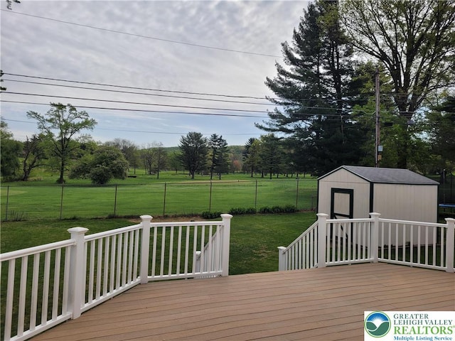 deck featuring a lawn, fence, an outbuilding, and a storage unit