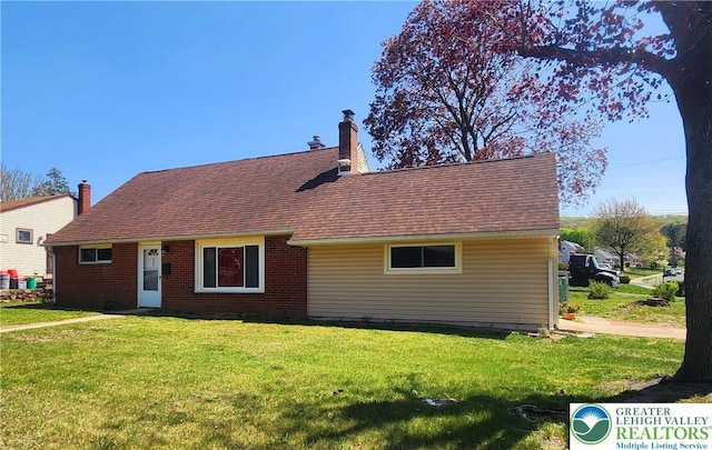 view of front facade featuring brick siding, a shingled roof, a front lawn, and a chimney