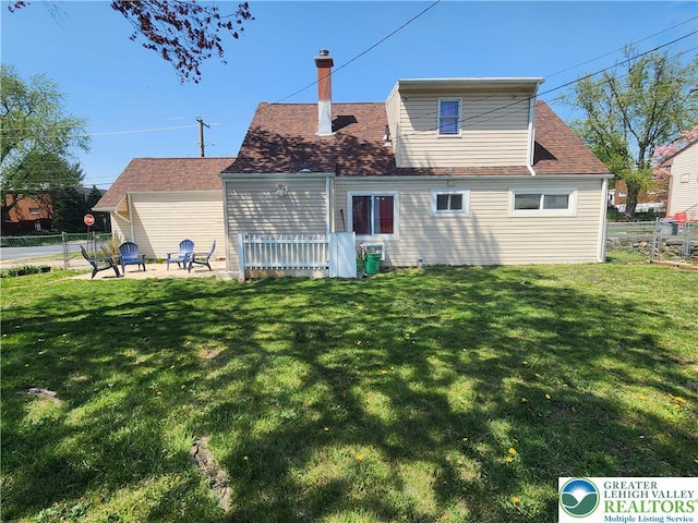 back of property with fence, a chimney, and a lawn