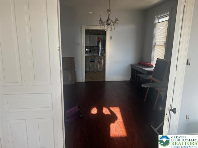 hallway featuring an inviting chandelier, baseboards, and wood finished floors