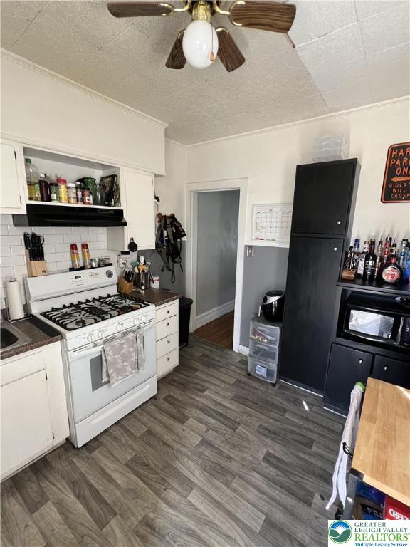 kitchen with dark countertops, white cabinets, a ceiling fan, and white range with gas cooktop