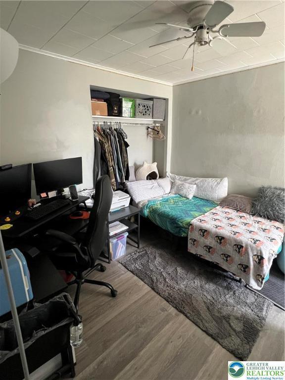 bedroom with a closet, ornamental molding, a ceiling fan, and wood finished floors
