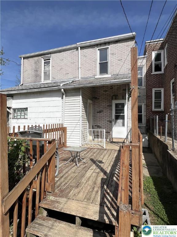 back of house featuring fence, a deck, and brick siding