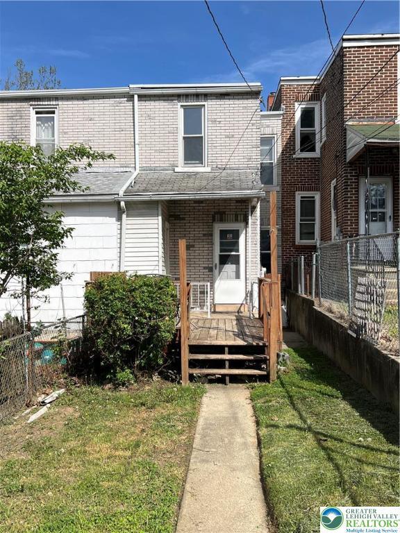 view of front of property with brick siding, fence, a wooden deck, and a front yard