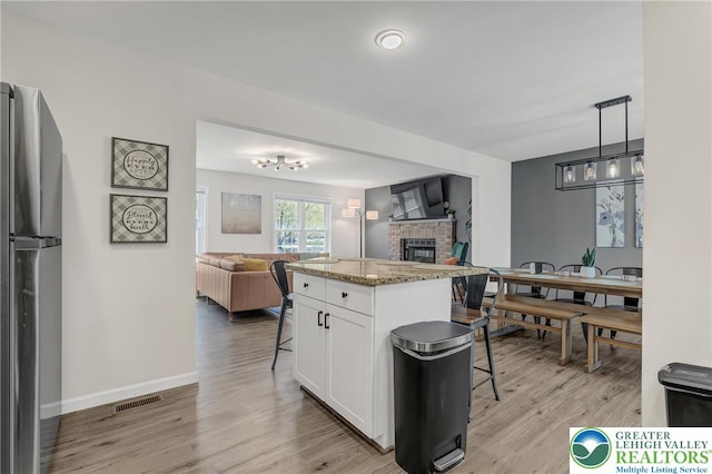 511 Lakeside Dr, Stroud Twp, PA 18301 - kitchen featuring a brick fireplace, white cabinets, freestanding refrigerator, open floor plan, and a breakfast bar