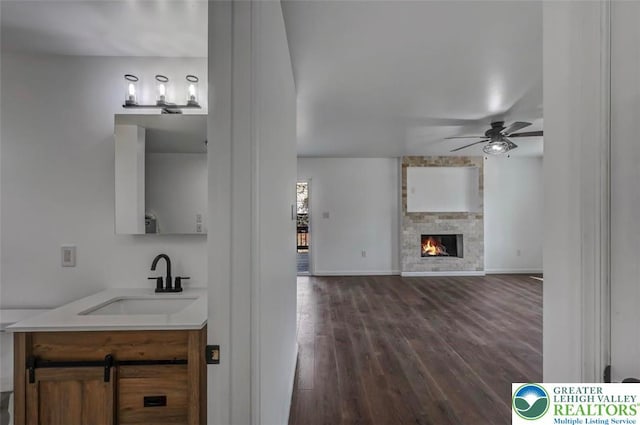 interior space featuring vanity, wood finished floors, a stone fireplace, baseboards, and ceiling fan