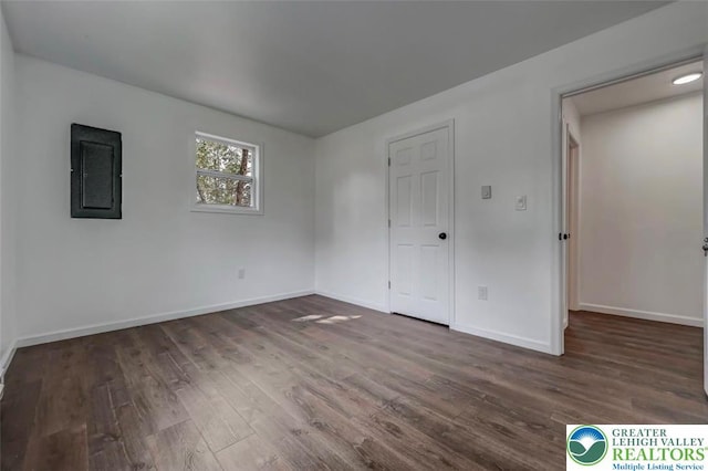 spare room with baseboards, electric panel, and wood finished floors