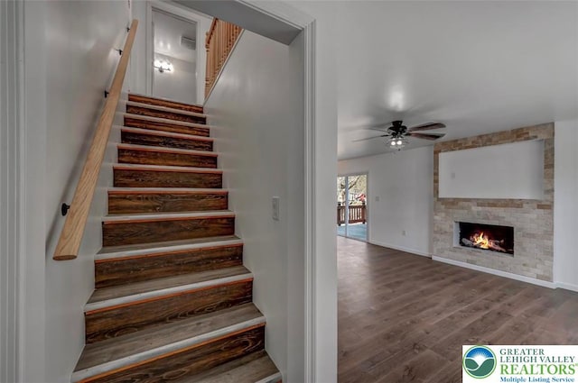 stairway with baseboards, ceiling fan, a fireplace, and wood finished floors