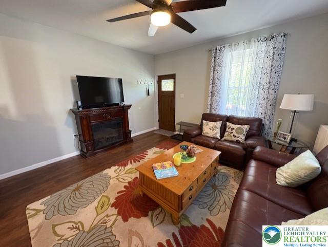 living area featuring baseboards, a glass covered fireplace, ceiling fan, and wood finished floors