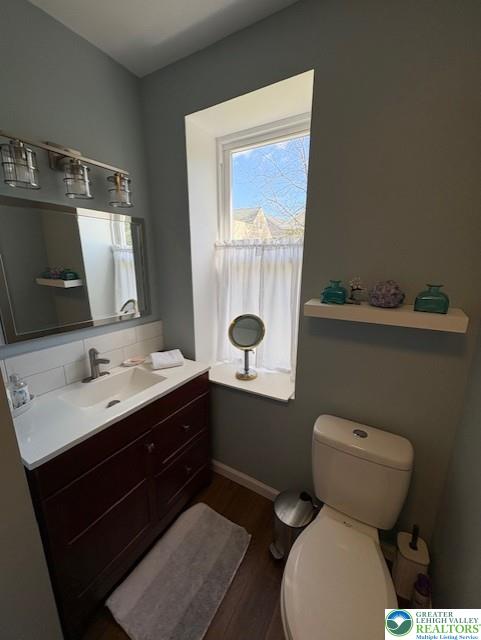 half bathroom featuring tasteful backsplash, wood finished floors, vanity, baseboards, and toilet