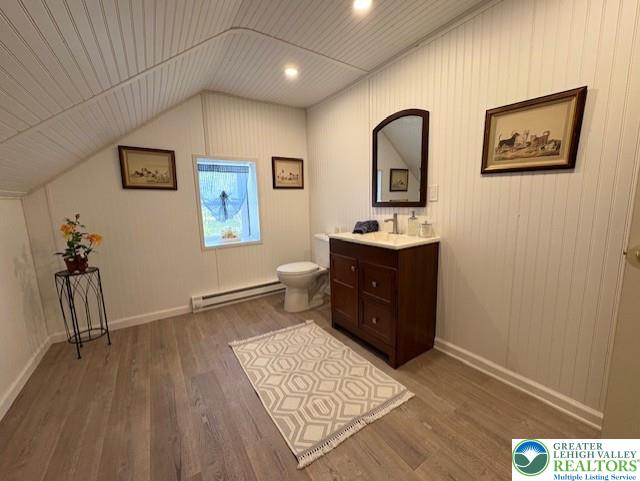 bathroom with a baseboard radiator, vaulted ceiling, toilet, and wood finished floors