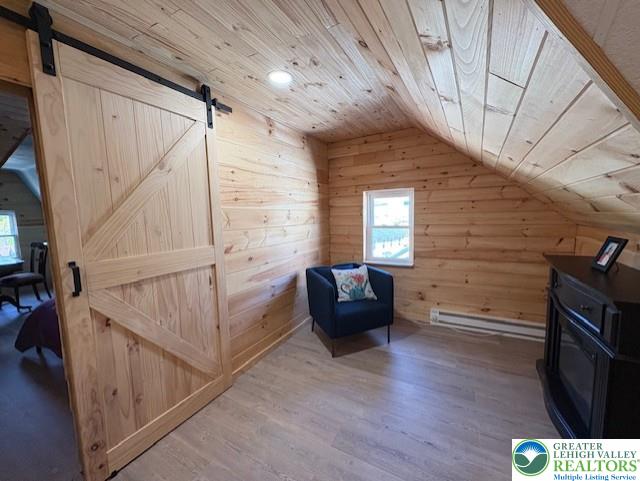 sitting room with wood finished floors, lofted ceiling, wooden walls, a barn door, and wooden ceiling
