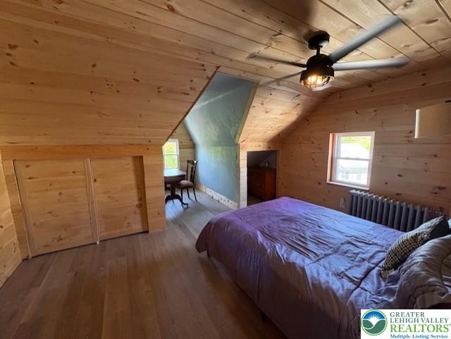 bedroom with wood-type flooring, radiator, lofted ceiling, wooden walls, and wood ceiling