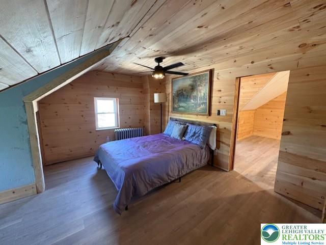 bedroom featuring radiator heating unit, wooden ceiling, wood walls, and wood finished floors
