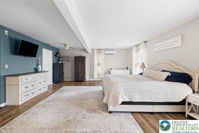 bedroom with baseboards, a wall unit AC, and wood finished floors