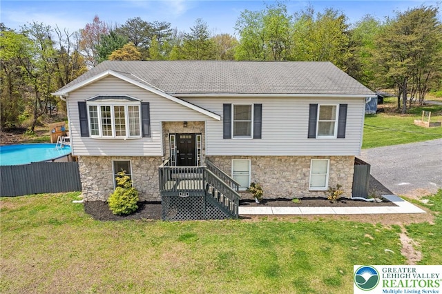 raised ranch with a front lawn, fence, and stone siding