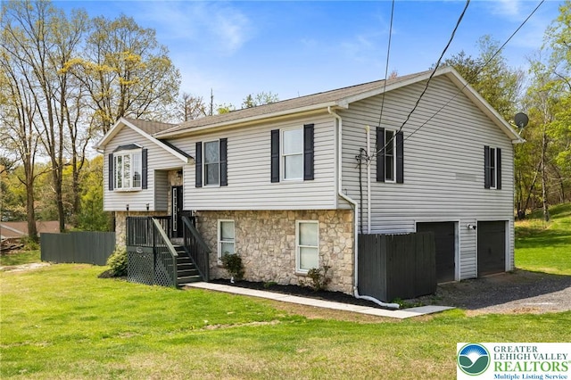 raised ranch with an attached garage, a front yard, driveway, and stone siding