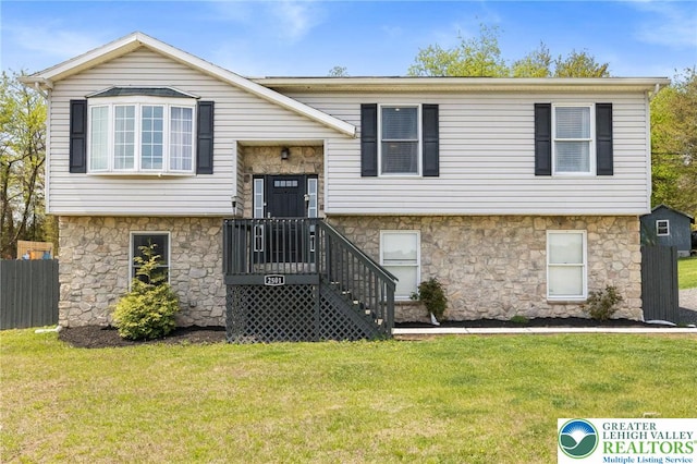raised ranch featuring fence, stone siding, and a front lawn