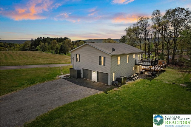 property exterior at dusk with a lawn, a garage, gravel driveway, and a deck