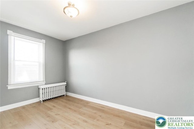 spare room with baseboards, radiator heating unit, and light wood-type flooring
