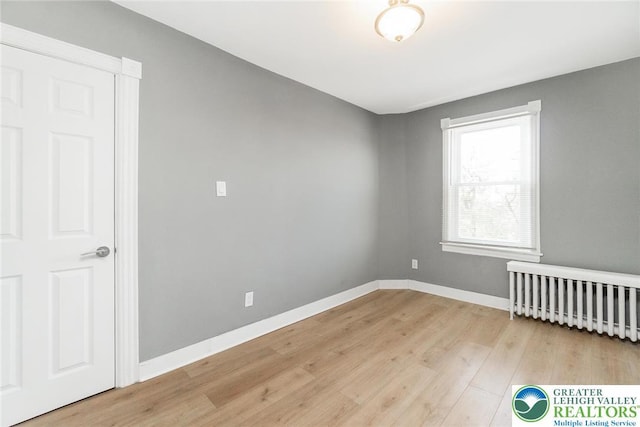 empty room featuring baseboards, radiator heating unit, and light wood-type flooring