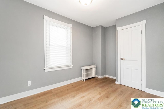spare room featuring radiator, baseboards, and light wood finished floors