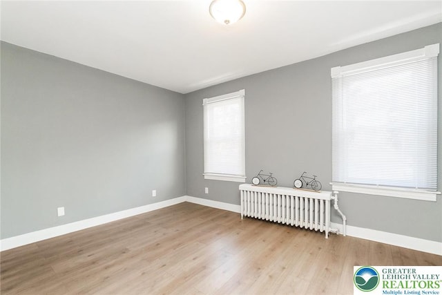 unfurnished room with radiator heating unit, baseboards, and light wood-type flooring