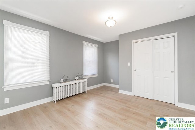 unfurnished bedroom featuring a closet, light wood-style flooring, radiator, and baseboards