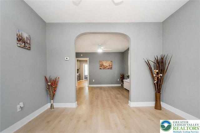 corridor featuring arched walkways, baseboards, and light wood-type flooring