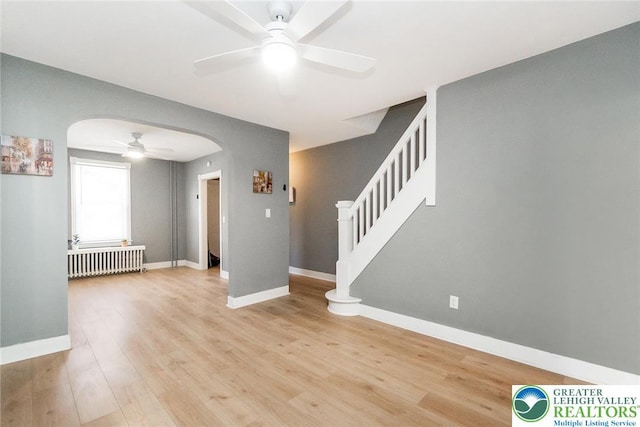 interior space featuring ceiling fan, arched walkways, baseboards, light wood finished floors, and radiator