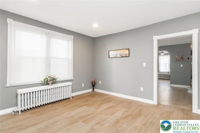 empty room featuring baseboards, radiator heating unit, and light wood finished floors
