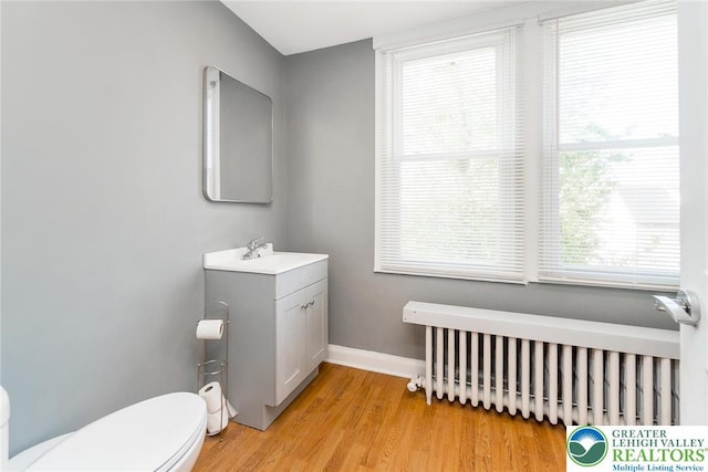bathroom with vanity, toilet, radiator, baseboards, and wood finished floors