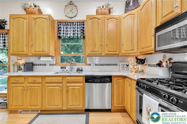 kitchen featuring appliances with stainless steel finishes, a sink, light wood finished floors, and tasteful backsplash