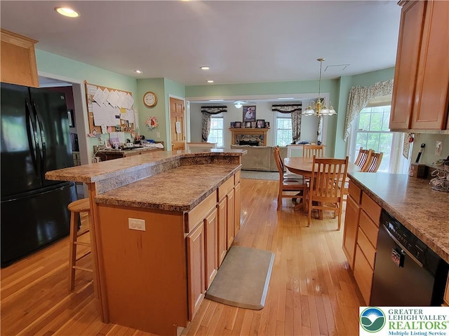 kitchen with a stone fireplace, a center island, freestanding refrigerator, dishwashing machine, and light wood-style flooring