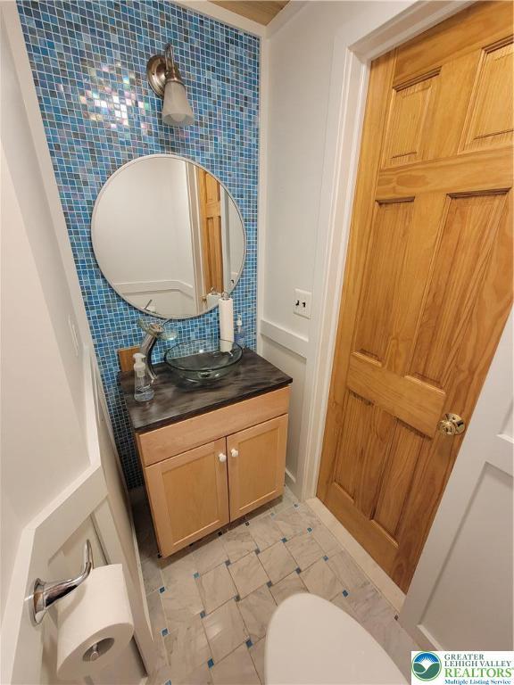 half bath featuring toilet, tasteful backsplash, and vanity
