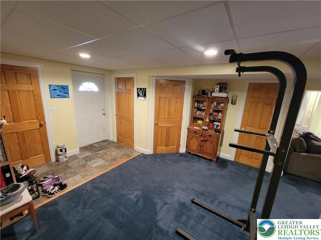 workout room featuring baseboards, a drop ceiling, and stone finish floor